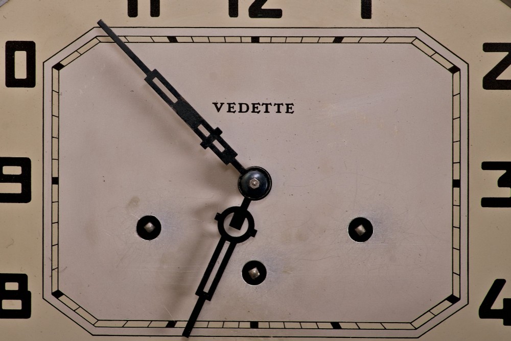 An Art Deco rectangular wooden wall clock featuring a light octagonal dial with Arabic numerals above a geometric leaded glass window. View V