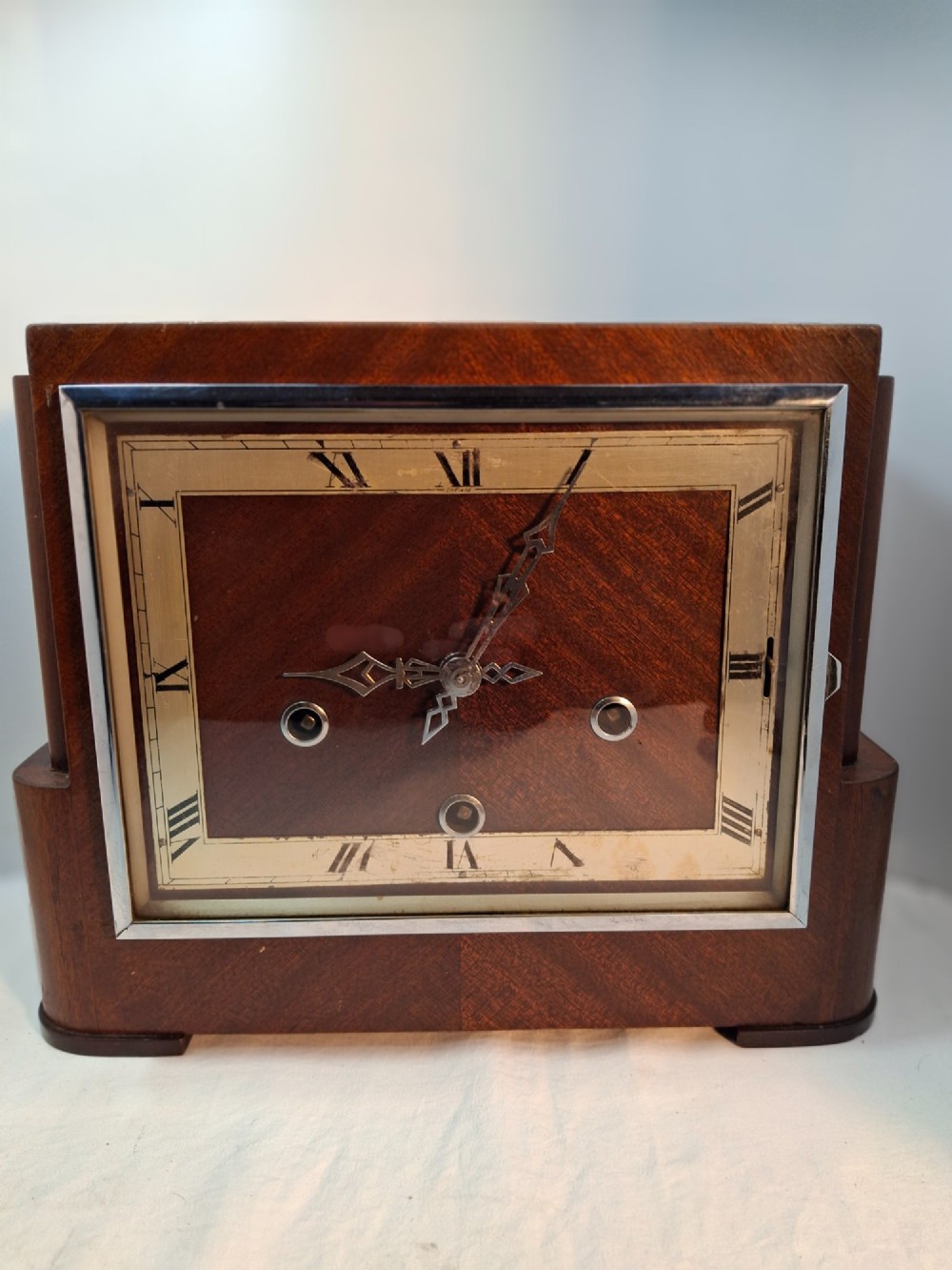 An Art Deco rectangular mantel clock crafted from rich brown walnut veneer featuring a silvered chapter ring with Roman numerals and a chrome-framed glass dial cover.