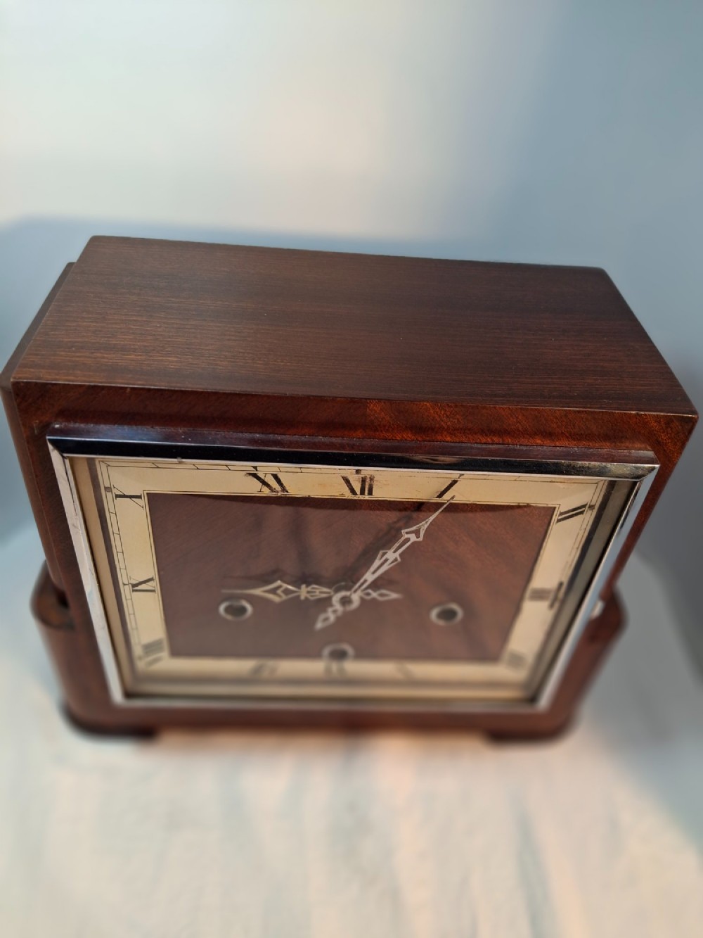 An Art Deco rectangular mantel clock crafted from rich brown walnut veneer featuring a silvered chapter ring with Roman numerals and a chrome-framed glass dial cover. View IV