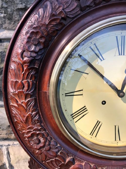 fig 1. A carved dark walnut drop dial wall clock featuring a circular Roman numeral dial above a glazed pendulum case flanked by turned side pillars.