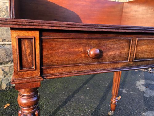 fig 1. A mahogany washstand featuring a raised gallery back, circular cutout aperture, two drawers with turned wood knobs, and turned reeded legs on brass castors.
