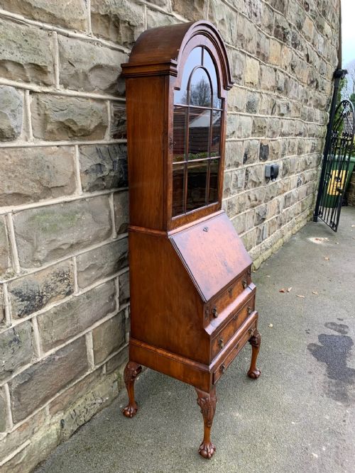 fig 1. A slim antique burr walnut bureau bookcase featuring an arched glazed top cabinet, a slant-front writing slope, three drawers, and carved cabriole legs with ball-and-claw feet.