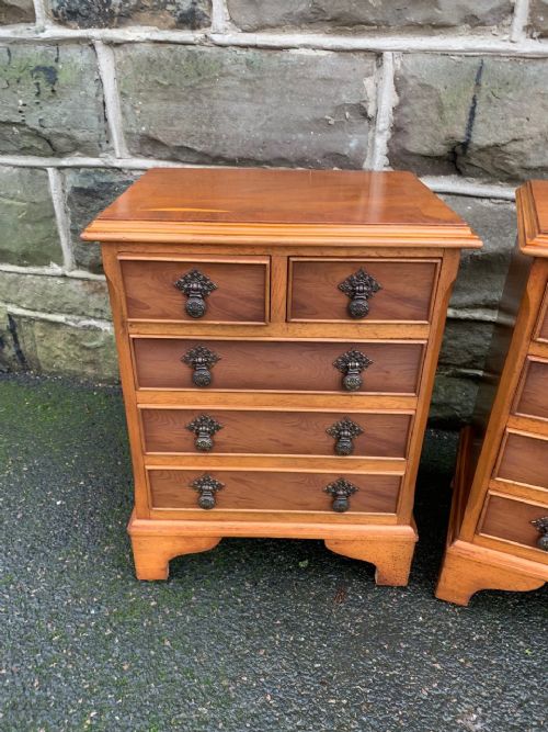 fig 1. A matching pair of warm brown yewwood bedside chests featuring four drawer fronts with ornamental brass drop handles and bracket feet.