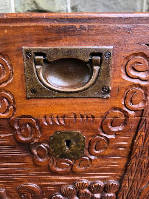 fig 1. A rectangular carved camphor wood chest featuring relief scenes of figures and oriental architecture with brass corner brackets.
