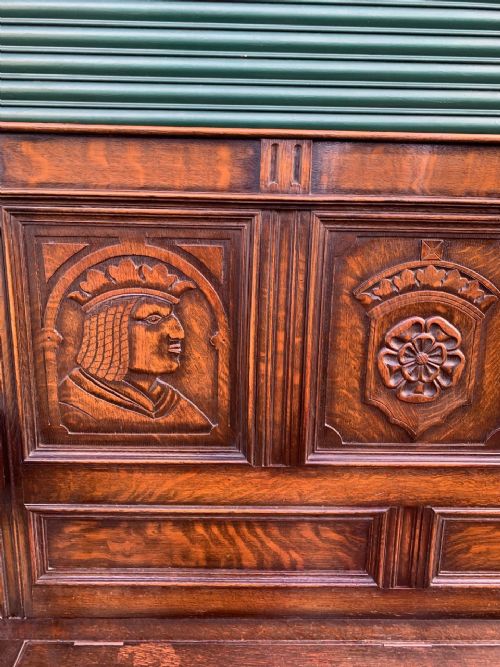 fig 1. A solid oak carved hall settle featuring a high panelled back with relief portrait carvings, curved armrests, and a box storage seat base.
