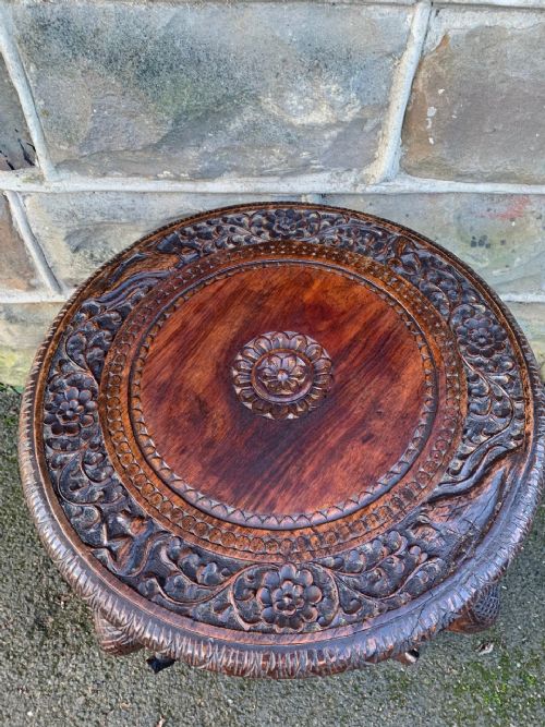 fig 1. A circular carved dark hardwood Anglo-Indian table featuring legs shaped like elephant heads with carved trunks and inlaid tusks.