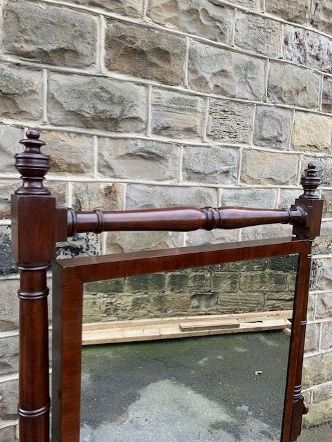 fig 1. An antique mahogany cheval mirror featuring a rectangular tilting glass frame, turned upright supports with finials, and reeded splayed legs on brass castors.