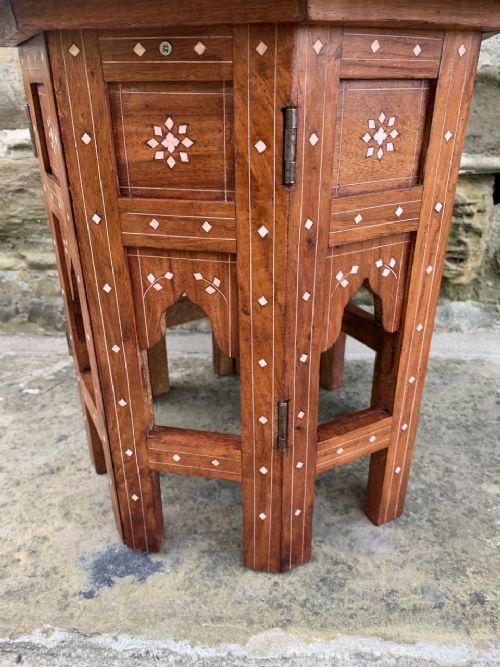 fig 1. A circular warm brown hardwood side table with intricate white bone floral and elephant inlay, featuring an octagonal collapsible base with carved archways.