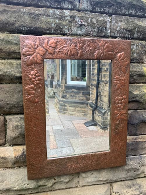 fig 1. A rectangular wall mirror featuring a hammered copper frame decorated with embossed repousse vine leaves and grape bunches.
