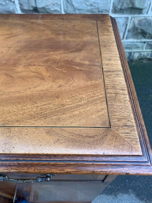 fig 1. An antique dwarf breakfront mahogany sideboard featuring a central stack of drawers flanked by cupboard doors with oval flame mahogany veneers and brass handles.
