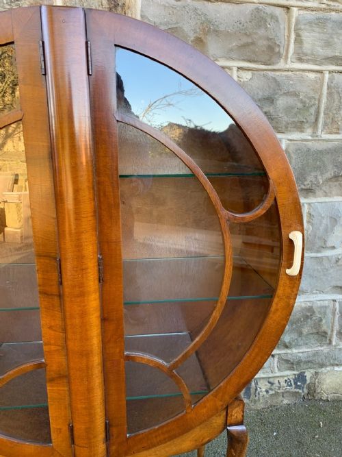 fig 1. An Art Deco circular walnut display cabinet featuring two glazed doors with geometric astragal bars, glass interior shelves, pale handles, and cabriole legs.