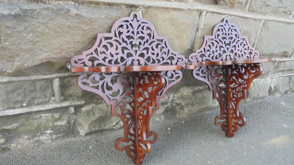 A pair of carved walnut wall brackets featuring pierced fretwork scroll designs and flat top display surfaces.