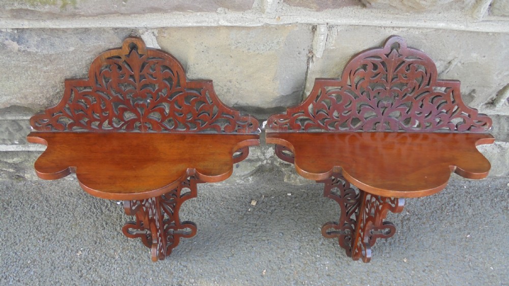 A pair of carved walnut wall brackets featuring pierced fretwork scroll designs and flat top display surfaces. View IX