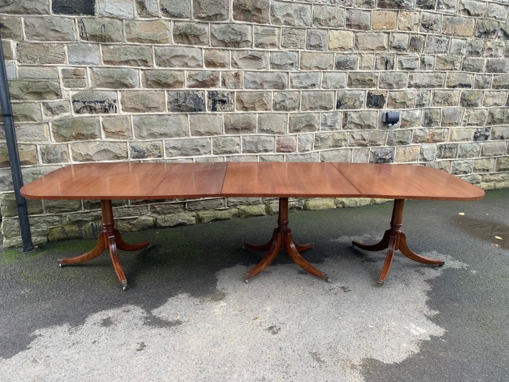 A long mahogany extending dining table supported by three pedestal bases with splayed legs and brass castors.