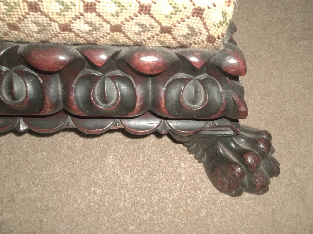 A low square William IV antique footstool with a deeply carved dark timber border, paw feet, and a beige patterned upholstered top. View II