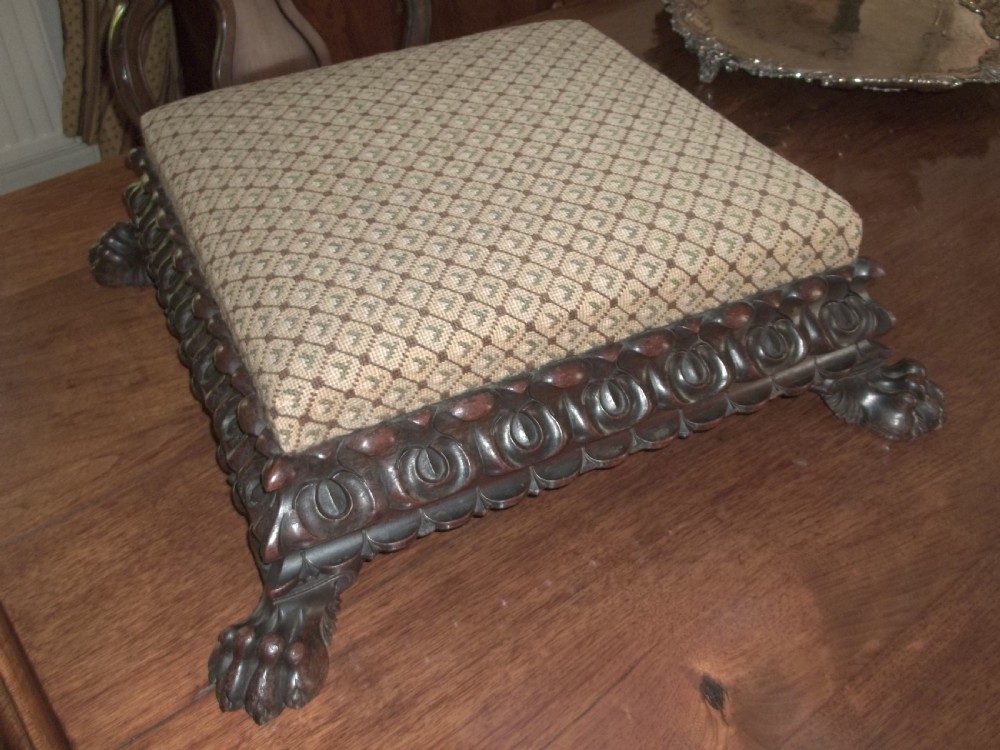 A low square William IV antique footstool with a deeply carved dark timber border, paw feet, and a beige patterned upholstered top. View III