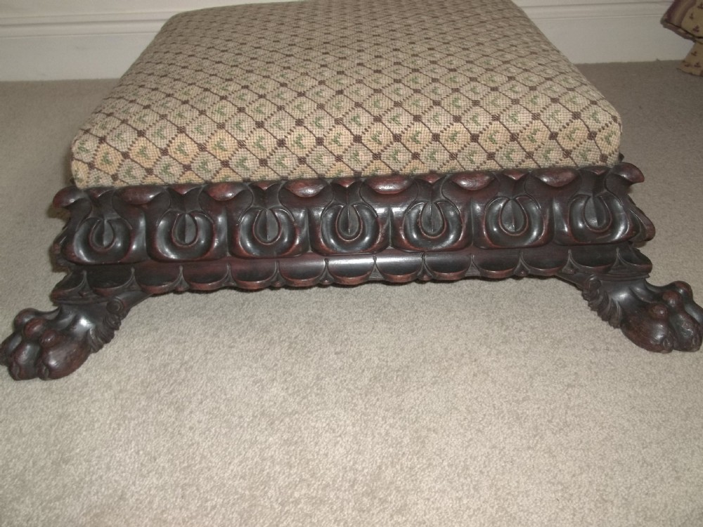 A low square William IV antique footstool with a deeply carved dark timber border, paw feet, and a beige patterned upholstered top. View IV