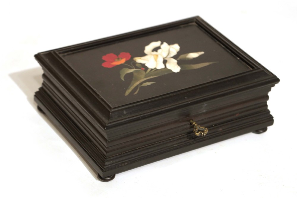 A 19th-century rectangular ebonised wood box featuring a pietra dura floral inlay of a white iris and red poppy on the lid, resting on small bun feet.
