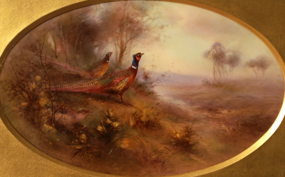 An oval-framed porcelain plaque featuring a hand-painted scene of two pheasants in a misty landscape, enclosed in a gold ornate frame. View II