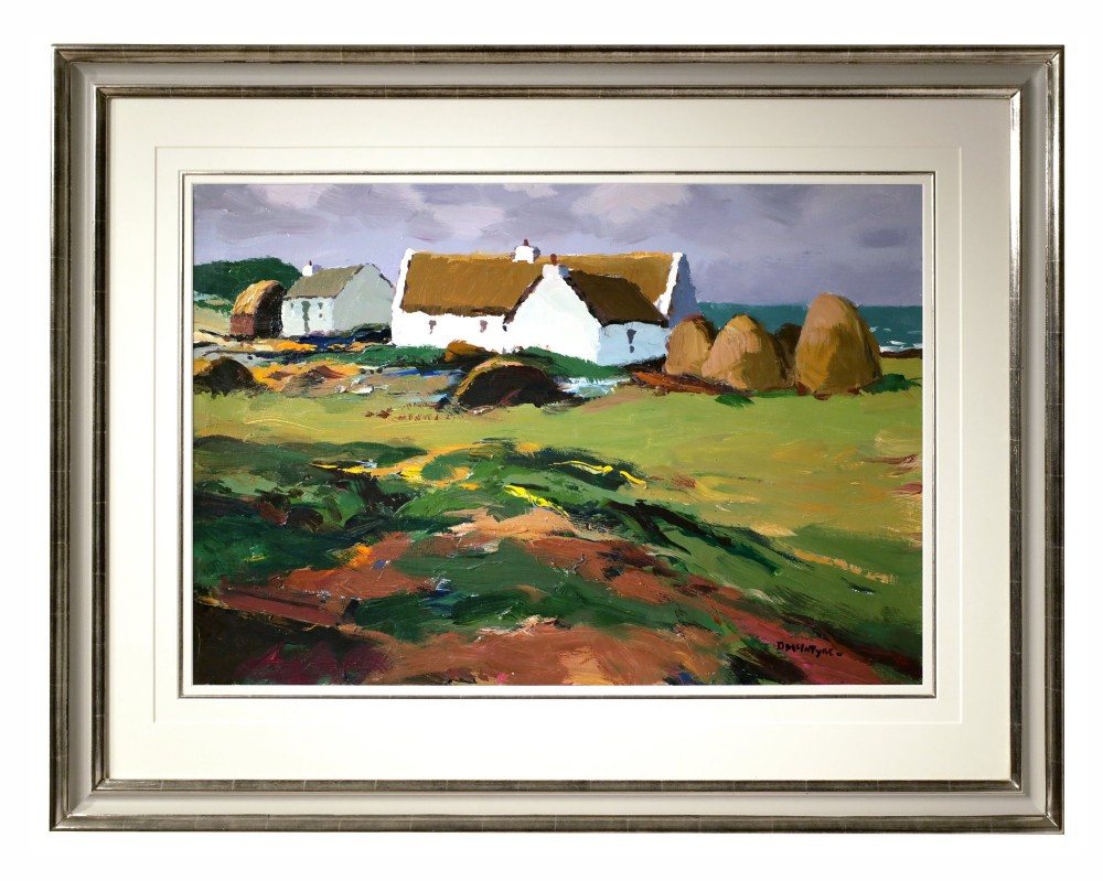 An original oil painting on board by Donald McIntyre depicting whitewashed coastal cottages with thatched roofs set in a green landscape, framed in a silver moulding.