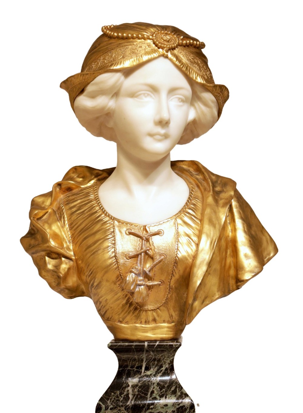 An Art Nouveau sculpture depicting a woman with a carved white alabaster face and neck, wearing a gilt bronze laced bodice and bonnet, set on a dark green veined marble base.