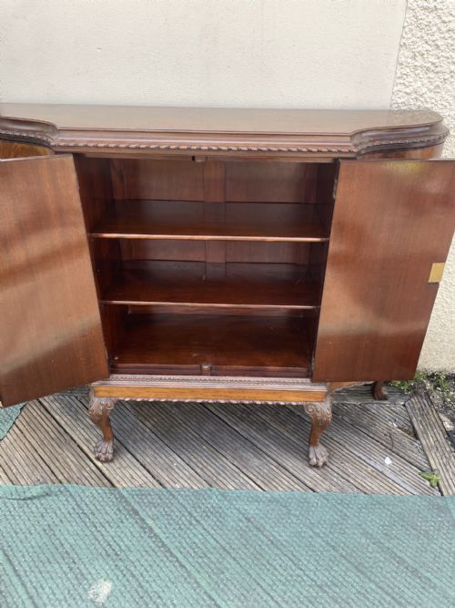 fig 1. A dark mahogany serpentine-front drinks cabinet featuring four doors, carved cabriole legs with ball-and-claw feet, and open internal shelving.