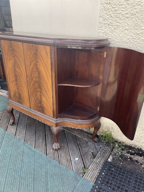 fig 2. A dark mahogany serpentine-front drinks cabinet featuring four doors, carved cabriole legs with ball-and-claw feet, and open internal shelving.
