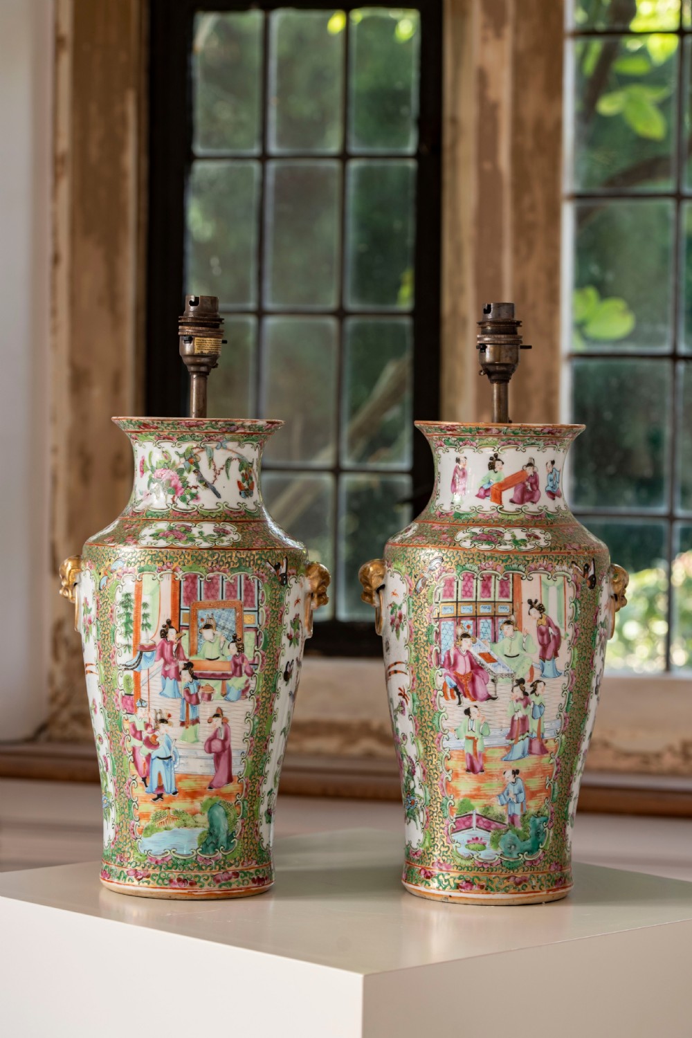 A pair of large Chinese Canton porcelain vase lamps with hand-painted polychrome figural panels, floral borders, and brass light fittings.