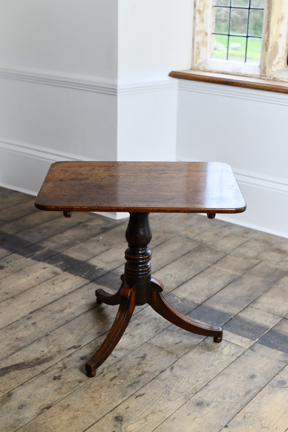 A Regency period mahogany tripod table featuring a square top with rounded corners, a central turned column, and three swept sabre legs. View II