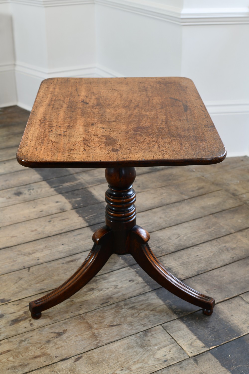 A Regency period mahogany tripod table featuring a square top with rounded corners, a central turned column, and three swept sabre legs.