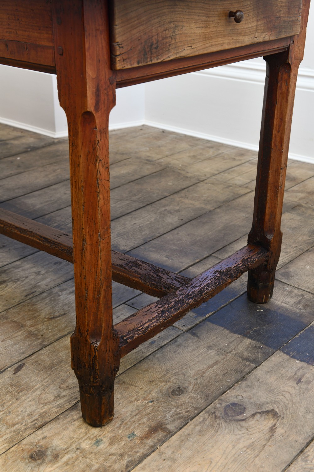 A long 19th-century rustic elm kitchen table featuring a plank top, a small end drawer, square legs, and a sturdy stretcher base. View VI