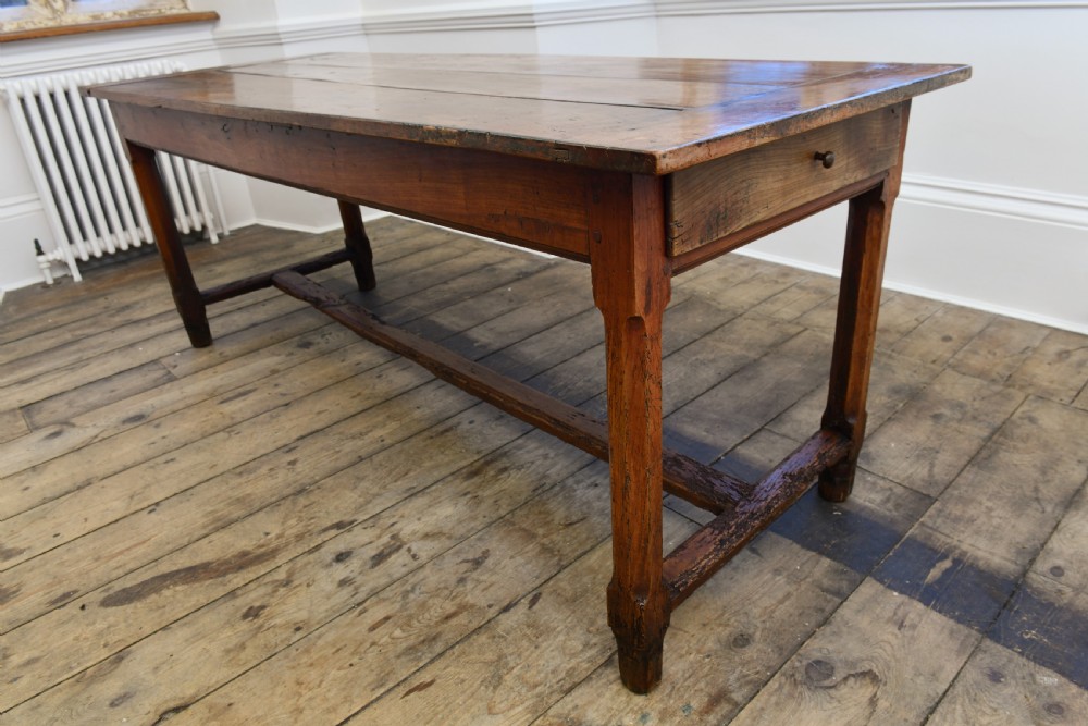 A long 19th-century rustic elm kitchen table featuring a plank top, a small end drawer, square legs, and a sturdy stretcher base. View VII