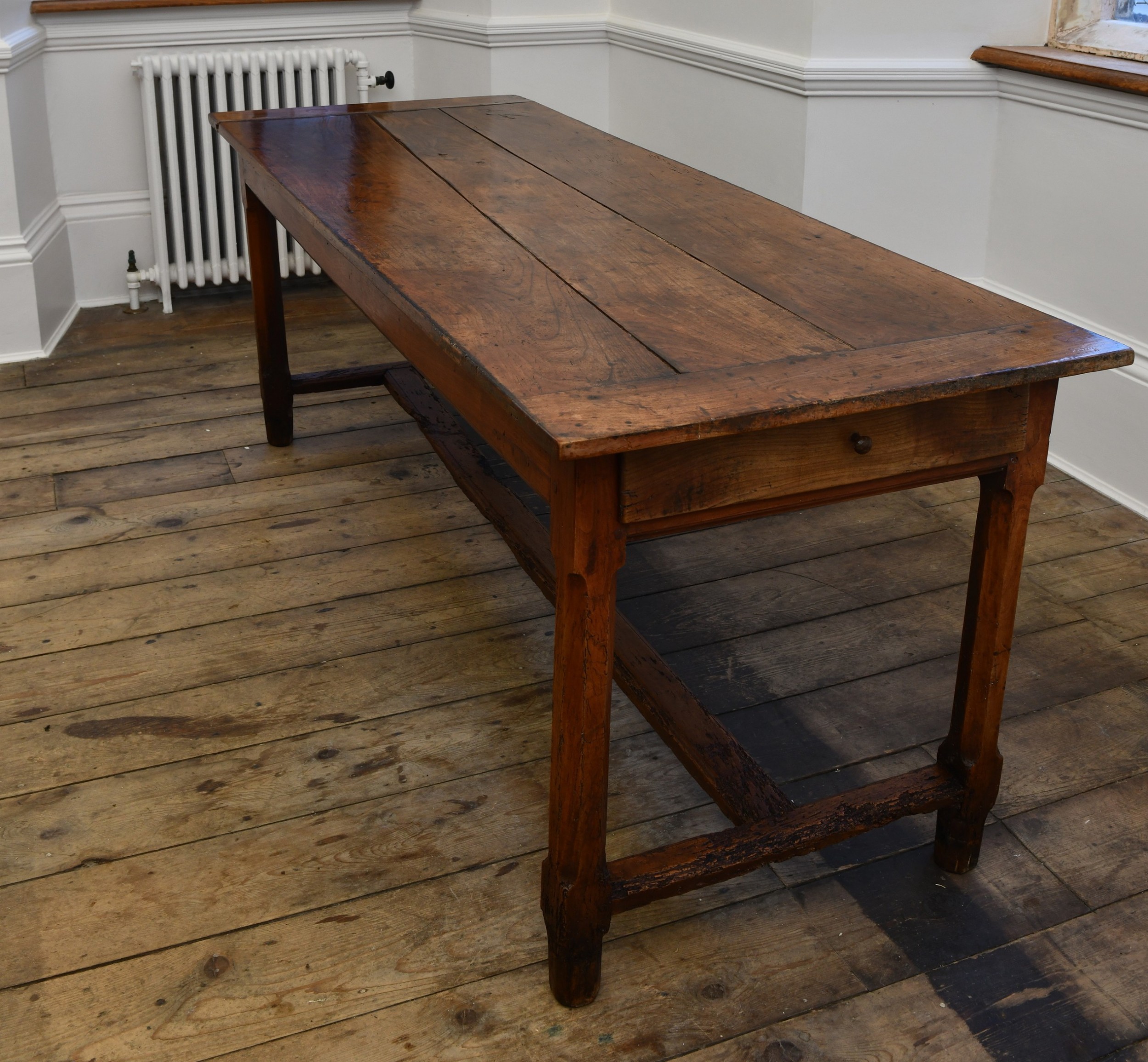 A long 19th-century rustic elm kitchen table featuring a plank top, a small end drawer, square legs, and a sturdy stretcher base.