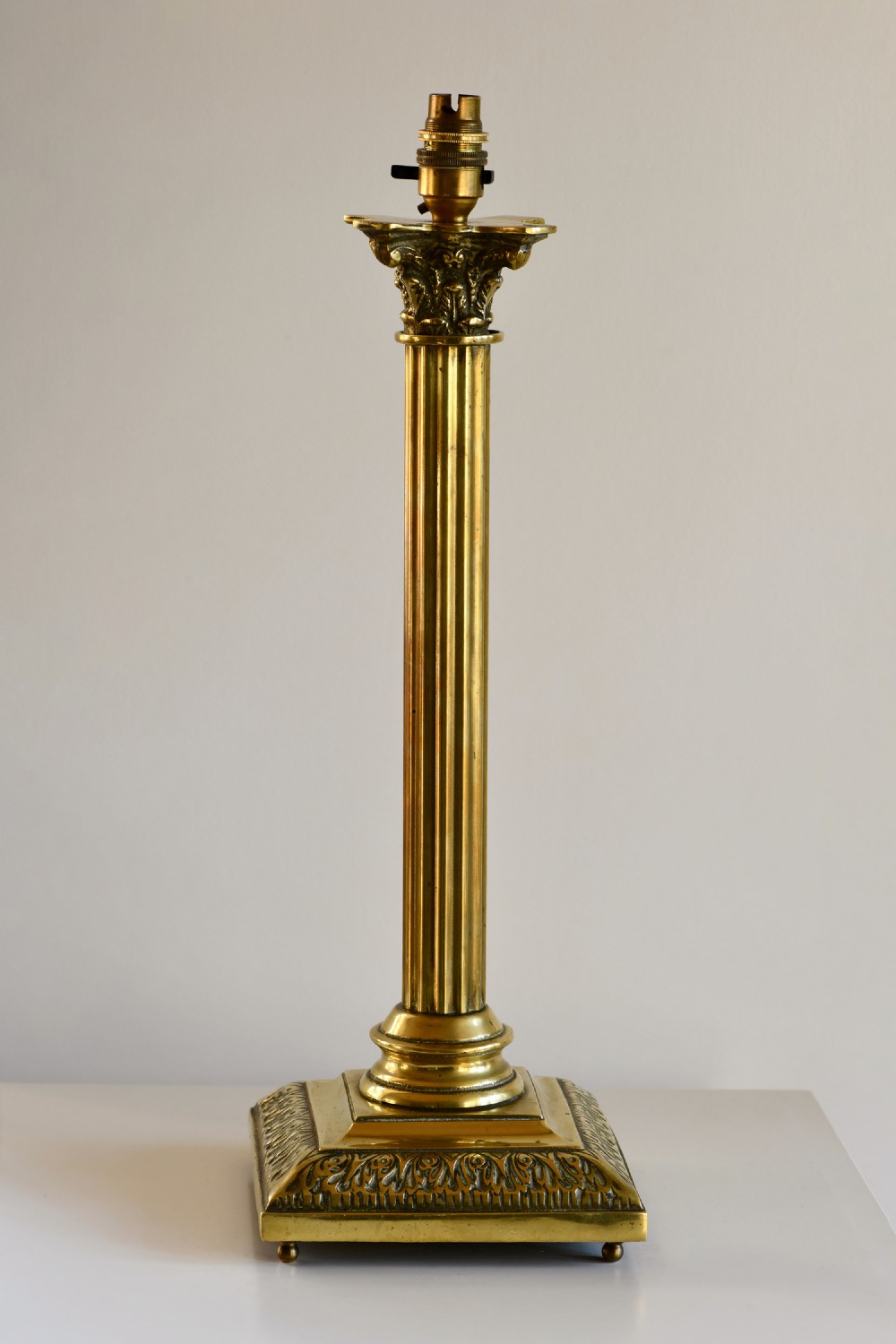 An Edwardian cast brass table lamp base featuring a central fluted column, a Corinthian capital, and an embossed square stepped base.