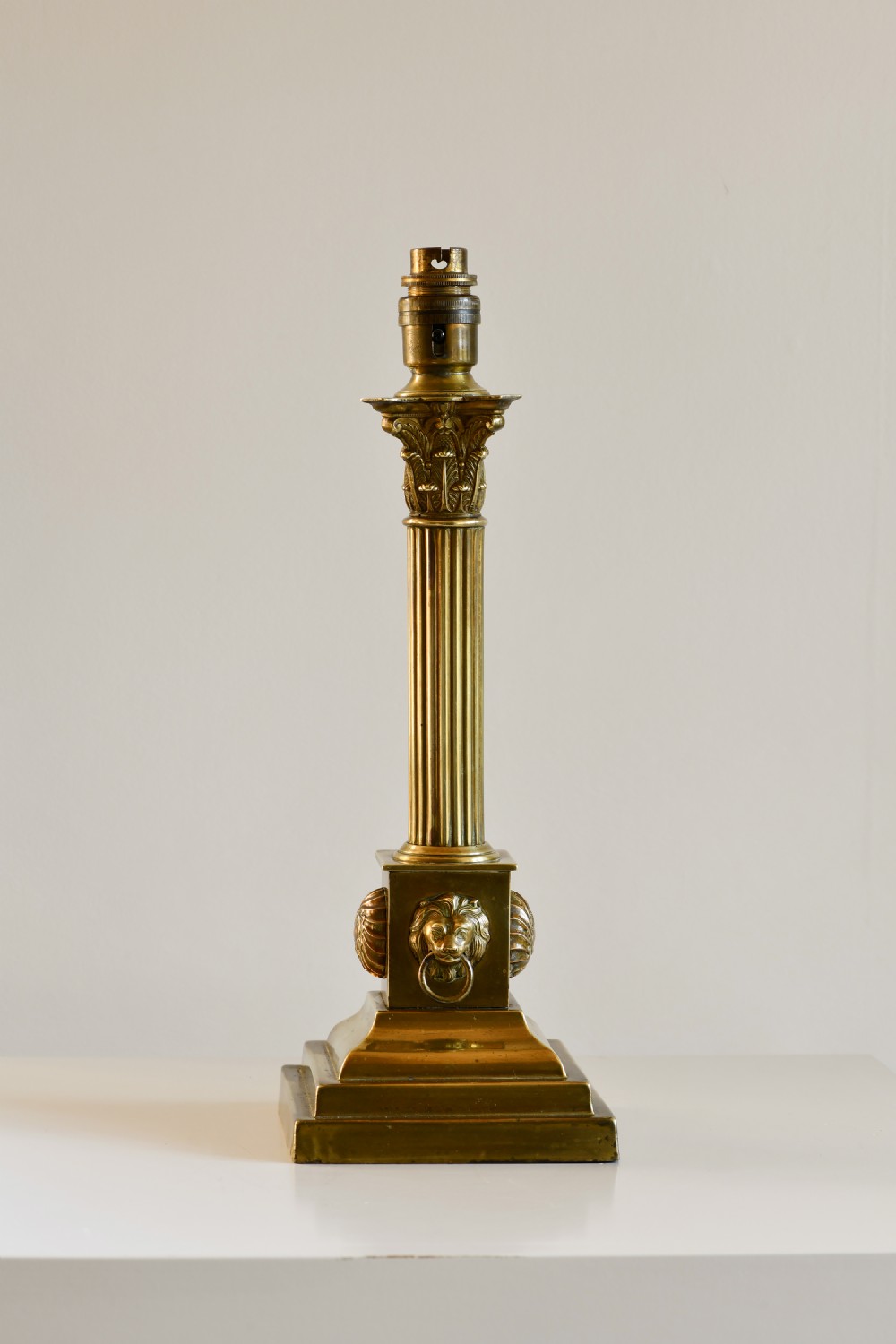 A late 19th-century brass table lamp styled as a fluted Corinthian column with lion mask motifs on a stepped pedestal base.