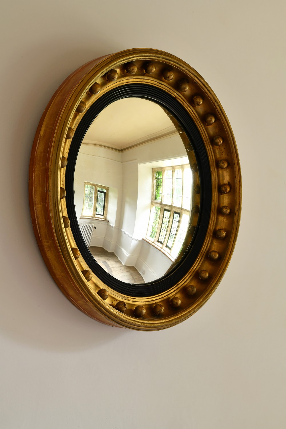 A large circular Regency period giltwood convex mirror featuring a ball-embellished frame and ebonised inner slip.