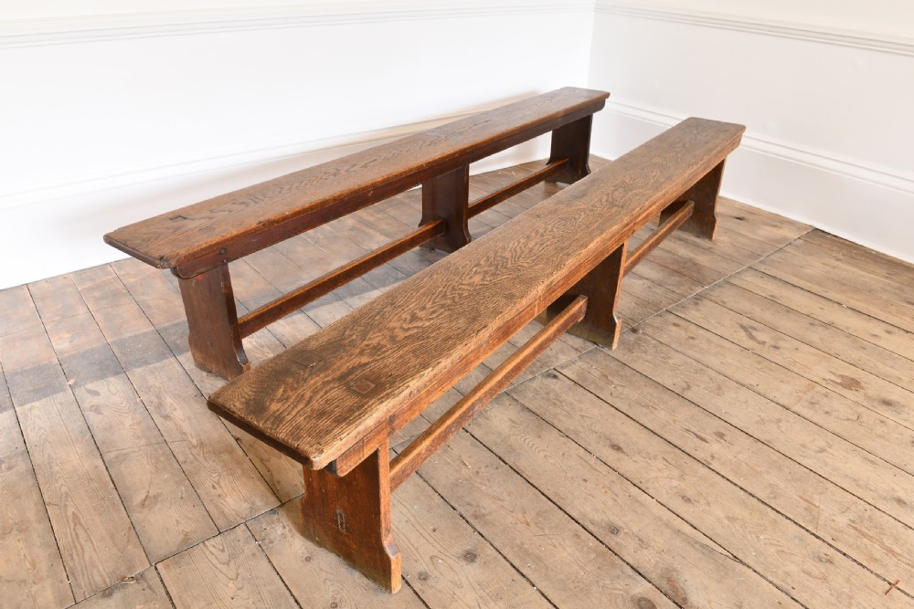 A pair of long solid brown oak benches featuring slab-end legs, exposed joinery, and central support stretchers.