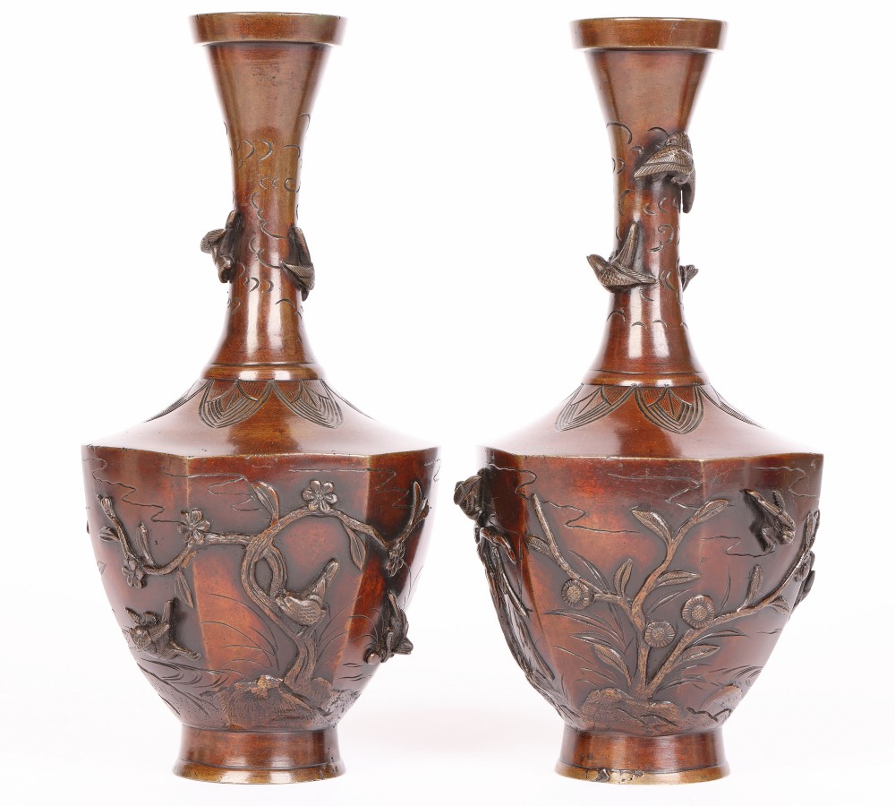 A pair of patinated bronze vases with flared necks and hexagonal bases decorated with high-relief applied bird and floral motifs.