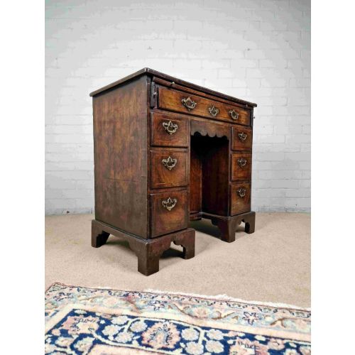 fig 1. An early Georgian warm brown walnut kneehole desk featuring brass drop handles, side drawers, a central recessed cupboard, and bracket feet.