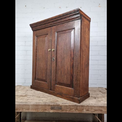 A late 18th-century Georgian oak wall cabinet featuring twin fielded panel doors, brass knobs, an escutcheon, and a moulded top cornice. View III