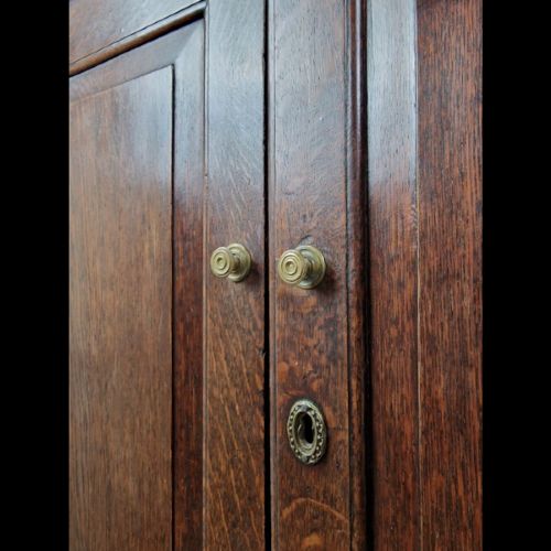 A late 18th-century Georgian oak wall cabinet featuring twin fielded panel doors, brass knobs, an escutcheon, and a moulded top cornice. View VII