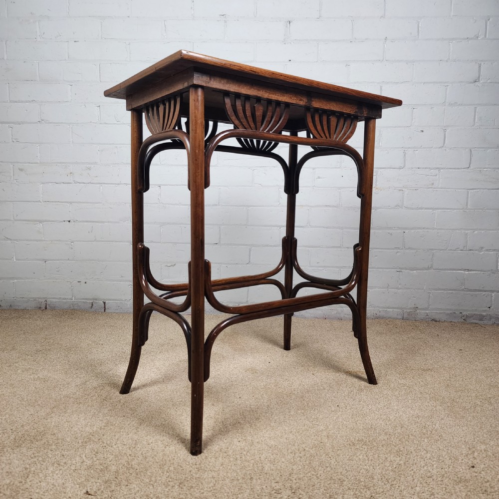 An Art Nouveau dark brown bentwood side table featuring carved palmette apron details and curved leg supports.