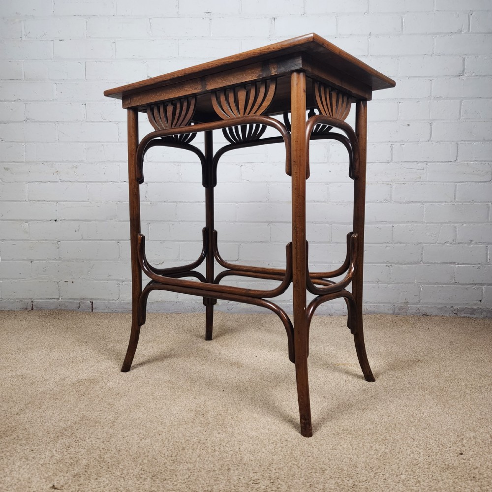 An Art Nouveau dark brown bentwood side table featuring carved palmette apron details and curved leg supports. View II