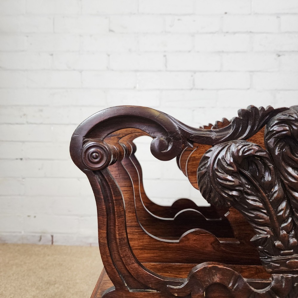 An early 19th-century carved rosewood Canterbury featuring vertical slatted partitions decorated with Prince of Wales feathers above a single base drawer with turned legs and brass castors. View II