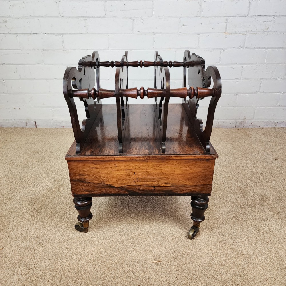 An early 19th-century carved rosewood Canterbury featuring vertical slatted partitions decorated with Prince of Wales feathers above a single base drawer with turned legs and brass castors. View III