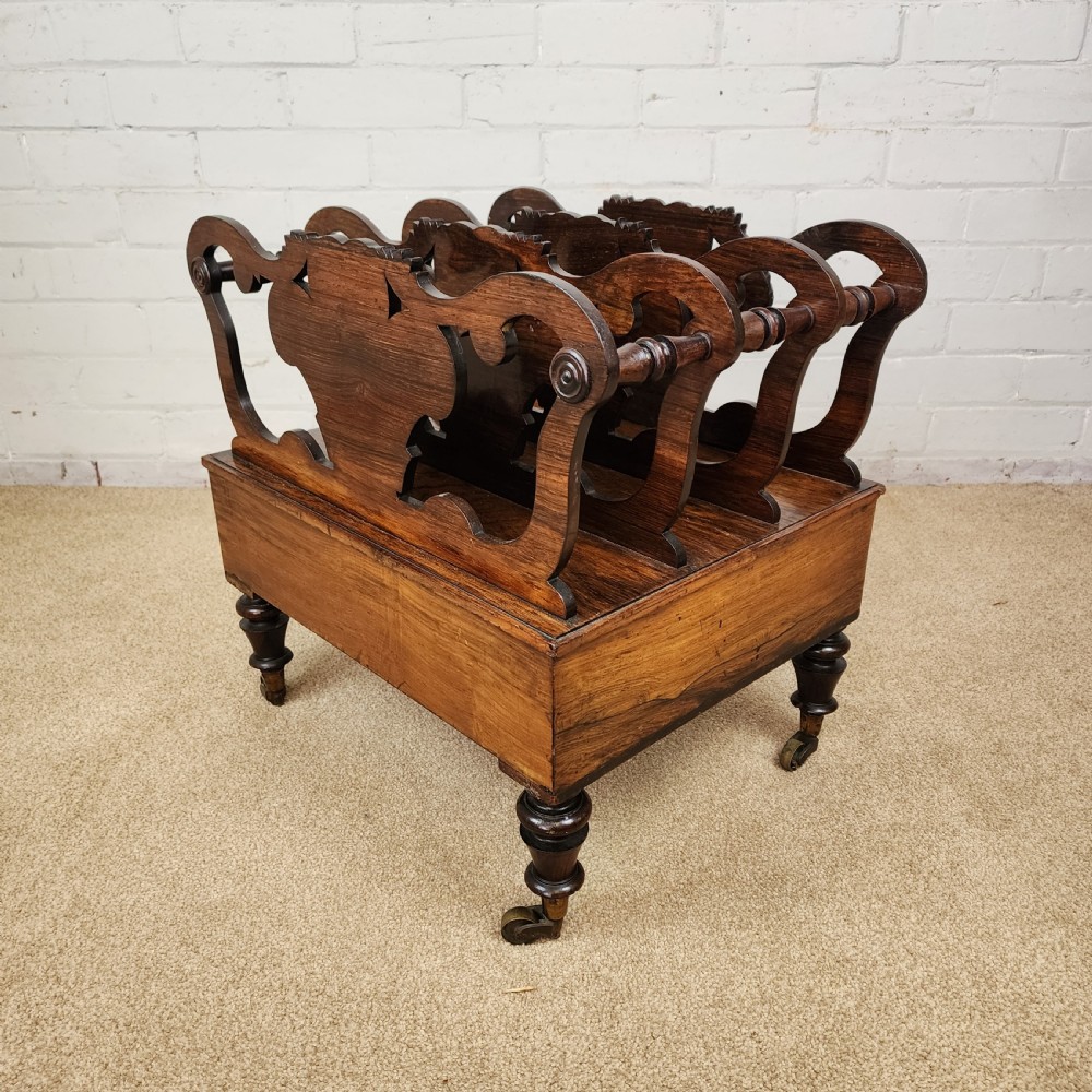 An early 19th-century carved rosewood Canterbury featuring vertical slatted partitions decorated with Prince of Wales feathers above a single base drawer with turned legs and brass castors. View IV