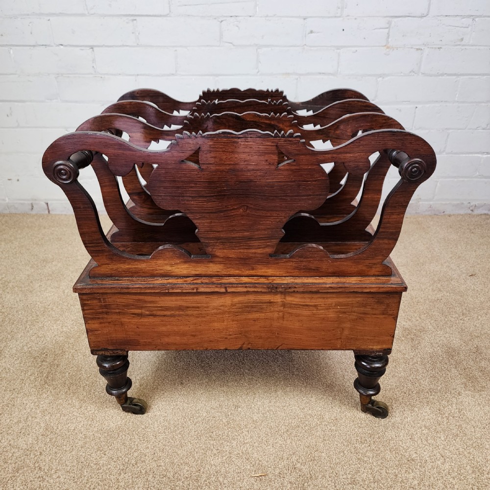 An early 19th-century carved rosewood Canterbury featuring vertical slatted partitions decorated with Prince of Wales feathers above a single base drawer with turned legs and brass castors. View V
