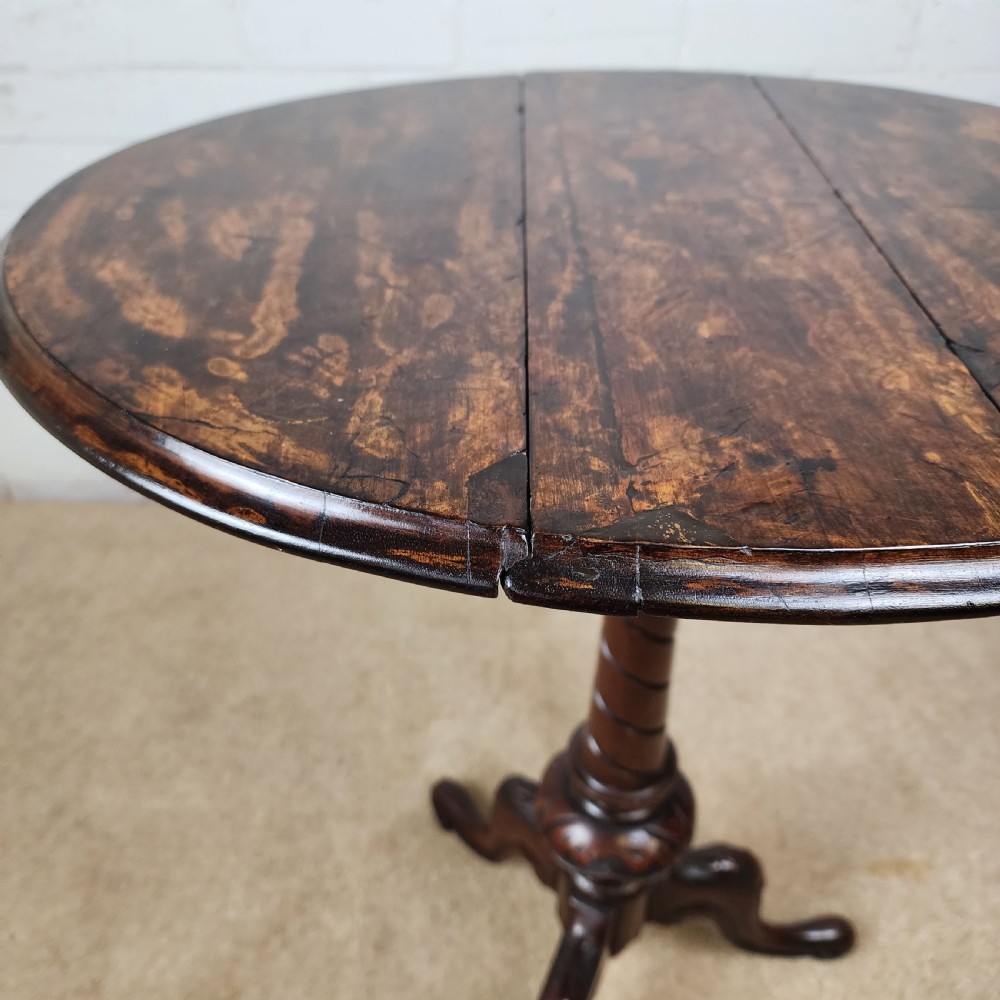 A Victorian circular occasional table made from dark burr walnut and mahogany, featuring drop leaves, a swivel top, a spiral carved central stem, and tripod carved feet. View V