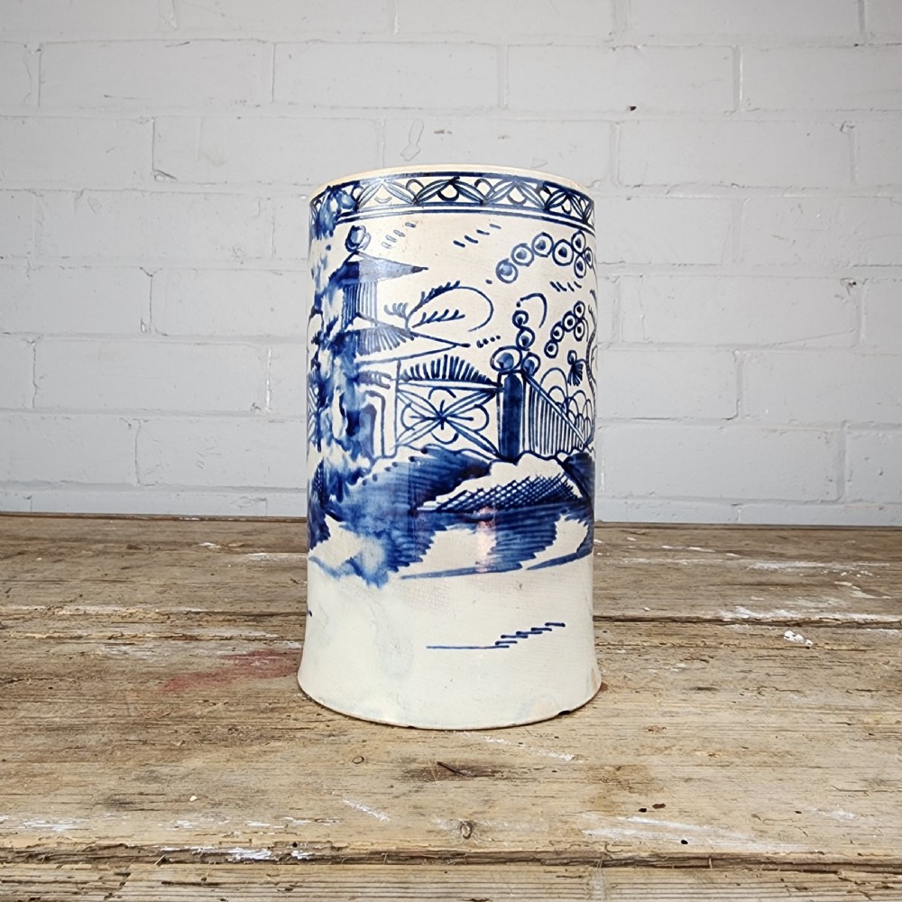An antique cylindrical ceramic mug featuring blue and white hand-painted chinoiserie landscape decoration and an applied handle. View II