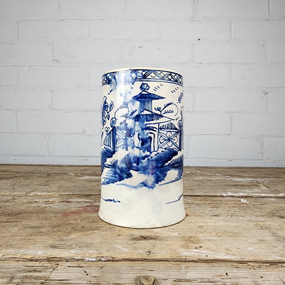 An antique cylindrical ceramic mug featuring blue and white hand-painted chinoiserie landscape decoration and an applied handle. View V